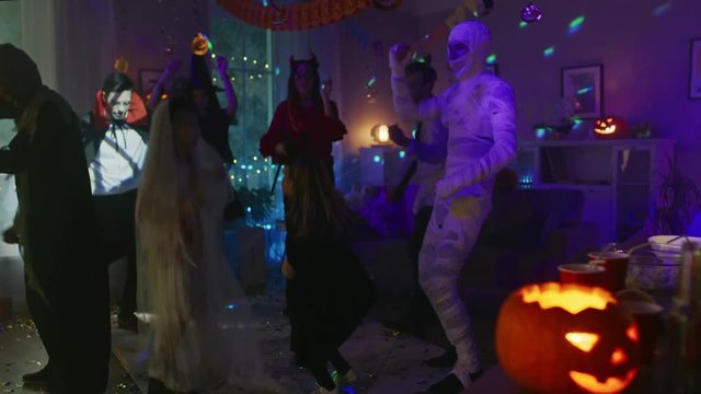 Halloween Costume Party:Group of Young Monsters Dancing and Having Fun in Decorated Room with Disco Lights. Zombie, Blood Thirsty Dracula, Mummy, Bewitching Witch, Dazzling She Devil and Little Bat