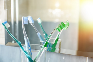 Toothbrushes in a glass vase in bathroom reflected in mirror