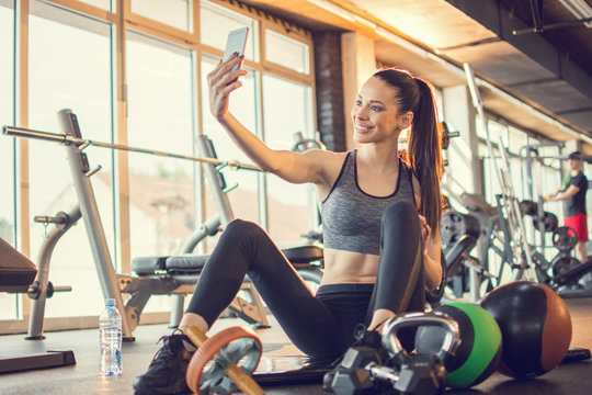 Beautiful girl in activewear using smart-phone to take a selfie photography during exercise break in gym