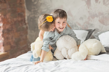 Brother and sister playing with teddy bear in bed