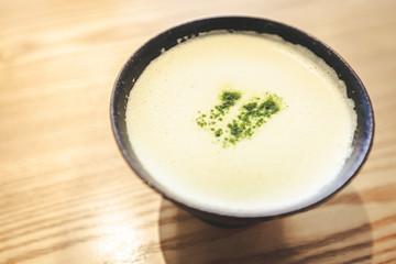 Close up of fresh brewed matcha latte with Japanese matcha green tea powder in black cup and stylish wooden table