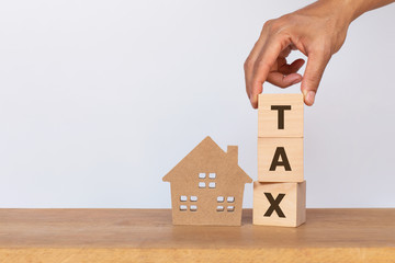 House model and wooden cubes with alphabet TAX on wooden table. Home taxes decrease concept