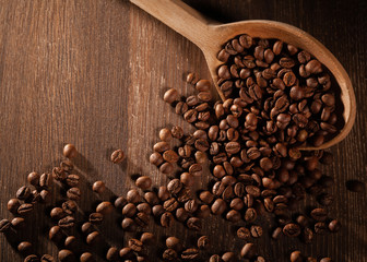 Scattered coffee beans with wooden spoons on wooden table.