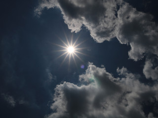A picture of bright sun among bright clouds on a sunny day.