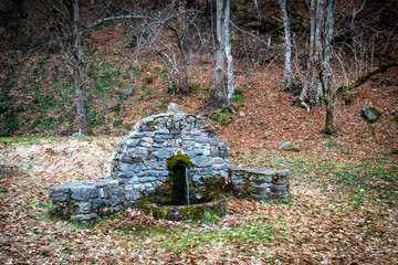 Old stone drinking fountain in the forest. End of winter and beginning of the spring