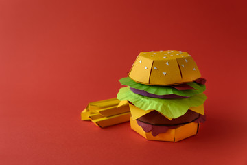 Paper cheeseburger with beef, cheese, tomato, lettuce, onion, bacon and fries on red background. Copy space. Creative or art food concept