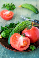 Fresh tomatoes and cucumbers on a round ceramic plate on an old wooden table.