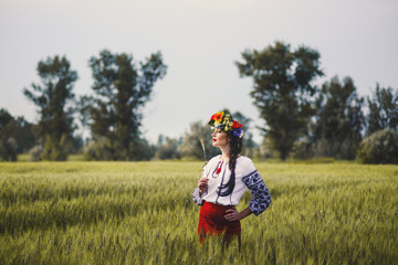 young beautiful woman with long hair in ukrainian national dress red skirt and a white shirt with a wreath of flowers in a field wheat
