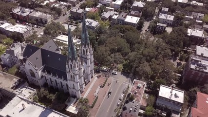 Aerial cinematic view of St Johns Cathedral, people, and horse cart in historic Savannah, Georgia.