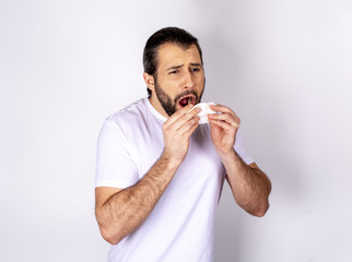 Handsome man in a white T-shirt on a white background, sneezes, caught a cold