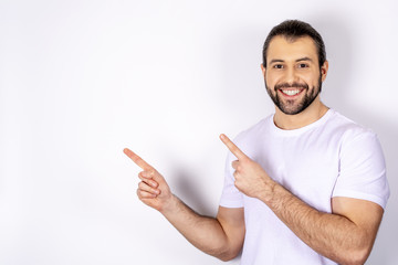 A handsome man in a white T-shirt on a white background, shows a finger to the side