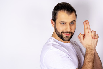 Fototapeta premium Handsome man in white t-shirt over white background, smiling, imitating with his hands a gun