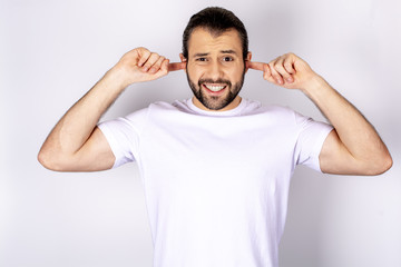 Fototapeta premium Handsome man in white t-shirt over white background, smiling, covering his ears with hands