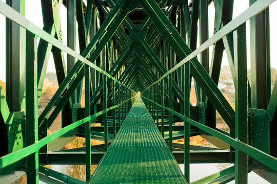 Metal structure of railway bridge, railway with vanishing point in the center. Trees on the background outside the bridge