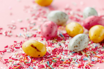 Obraz premium Easter chocolate eggs candy with colorful sprinkles on a pastel pink background, creative easter concept, top view