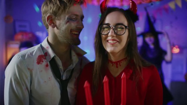 Halloween Costume Party: Brain Dead Zombie and Beautiful She Devil with Trident Dance as a Couple. In the Background Monsters Having Fun and Dancing in the Decorated Room