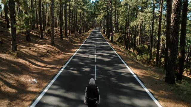 Inspirational and beautiful motivational drone shot of camera following young adventurous woman with hiking or camping backpack, walk in middle of road towards dreams and goals for blogger travel