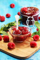 raspberry jam with fresh raspberries and mint. marmalade on spoon and jar on blue