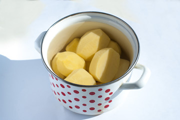 peeled raw potatoes in a pot on a white background