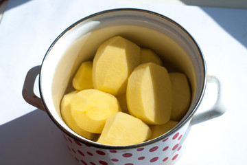 peeled raw potatoes in a pot on a white background