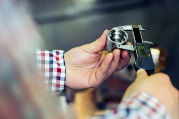 Naklejka premium Technician in a Metal Manufacturing Company Measuring with Digital Vernier Caliper 