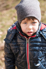 Vertical portrait of a sad little boy dressed in warm clothes and with a hat