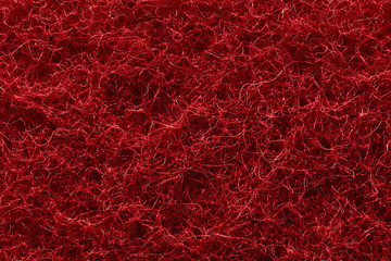 The texture of the surface of interwoven red threads of abrasive synthetic fiber.
