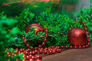 Red beads and toys for decorating the Christmas tree on a wooden background next to the coniferous branches