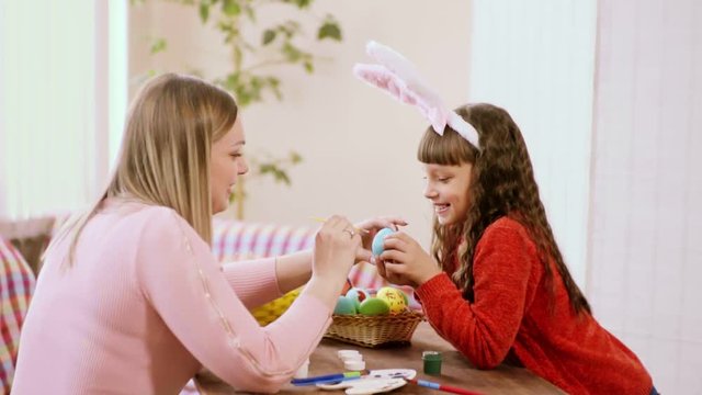 mom touches a brush to her daughter's nose, while coloring Easter eggs.