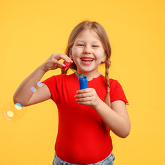 Cute little girl 5-6 years old blows bubbles and laughs in the studio on a yellow background