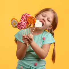 Cute little girl licks candy and laughs in the studio on a yellow background