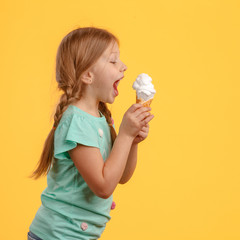 Cute little girl eats ice cream and laughs in studio over yellow background