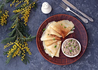 Thin pancakes on a clay brown plate. Served with forshmak, a snack made from chopped salted herring, eggs and onions. Top view.
