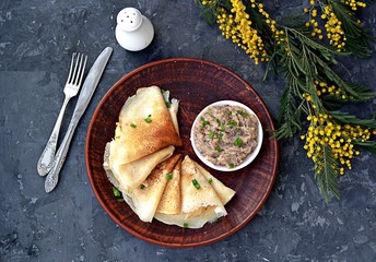 Thin pancakes on a clay brown plate. Served with forshmak, a snack made from chopped salted herring, eggs and onions. Top view.