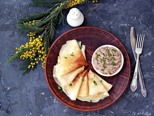 Thin pancakes on a clay brown plate. Served with forshmak, a snack made from chopped salted herring, eggs and onions. Top view.