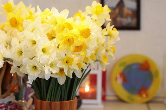  bouquet of yellow and white daffodils in a vase on the background of a candle, a yellow plate with tulips and painting