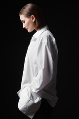 Portrait of an elegant young woman in a white shirt and black pants. Interesting studio light