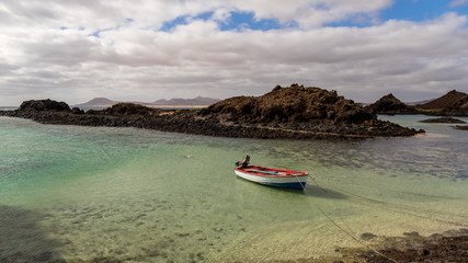 Fototapeta na wymiar Boat and volcanic landscape at the little port of Lobos island in Fuerteventura, Canary islands