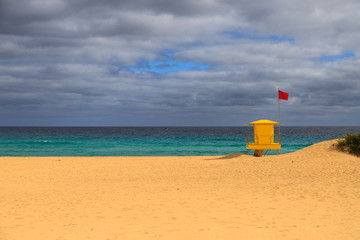 Beautiful yellow lifeguard tower on the beach with a red flag. Saturated colors on a cloudy day