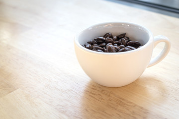 Roasted coffee beans in a white glass on a wooden table
