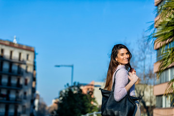Rear view of smiling beautiful young woman standing in the street while looking camera in a sunny day