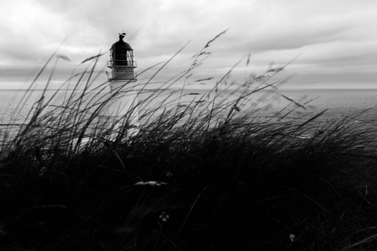 Top of Rua Reidh lighthouse with moving grass in the foreground and sea in the background, in black and white.