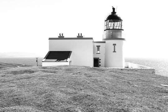 Small Stoer Head lighthouse with keepers house and bright sea in the background, in black and white.