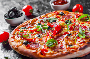 Pepperoni Pizza with Mozzarella cheese, salami, Tomatoes, olive, pepper, Spices and Fresh arugula. Italian pizza on dark background