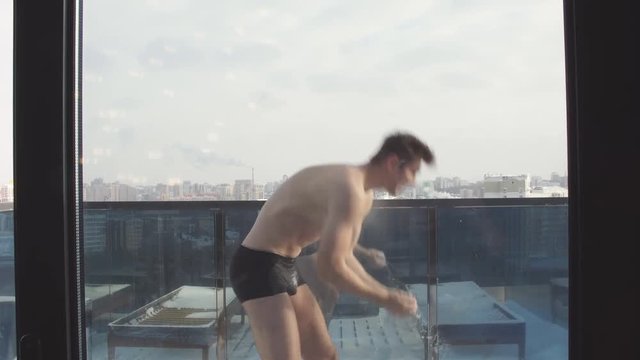 Half naked man in bathing shorts and bathrobe stands on top roof of skyscraper, getting fresh after steam-room of sauna