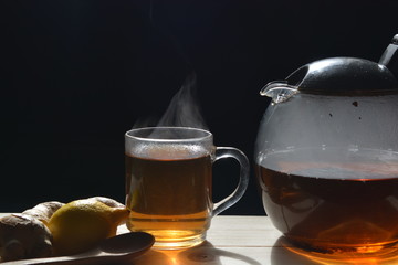 smoke rising from a cup of ginger tea with a teapot on a wooden table in front of a black background