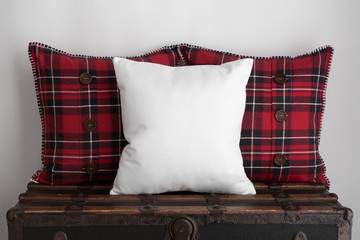 Mockup of a large white square cushion with two red plaid square cushions sitting on top of an old vintage suitcase.