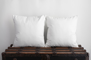 Mockup of two large white square cushions sitting on an old vintage suitcase