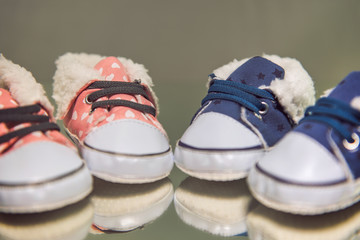 Two pairs of baby shoes, one for a boy and one for a girl are standing on a mirror in front of a...
