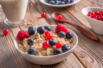 Close up view of porridge with blueberries and raspberries and grain bread on wooden background.